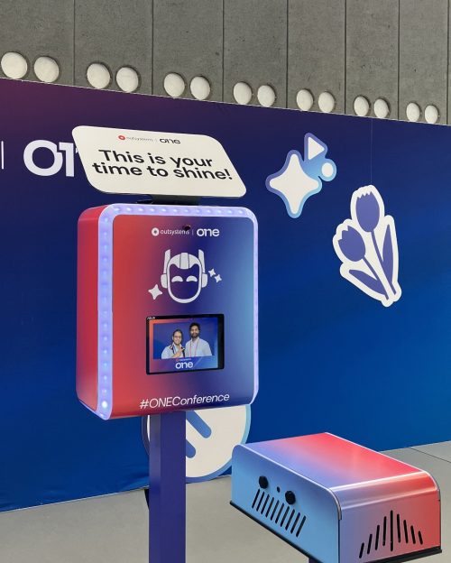 Branded photo booth wrap with OutSystems ONE logo and #ONEConference hashtag at corporate conference
